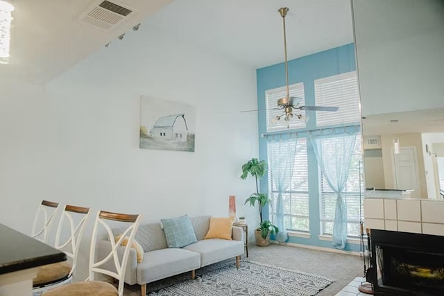 living room with carpet, visible vents, a tile fireplace, ceiling fan, and a towering ceiling