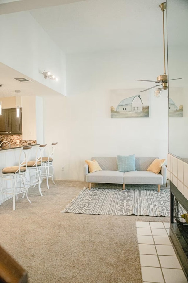 living area featuring visible vents, light colored carpet, a towering ceiling, and a ceiling fan