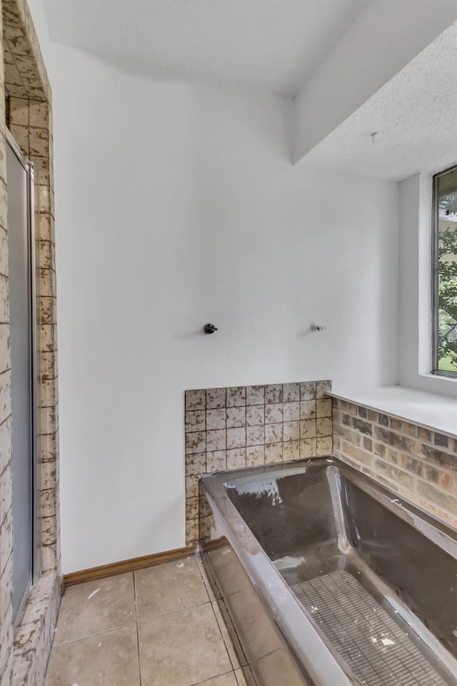 bathroom featuring tile patterned floors, a textured ceiling, a bath, and baseboards