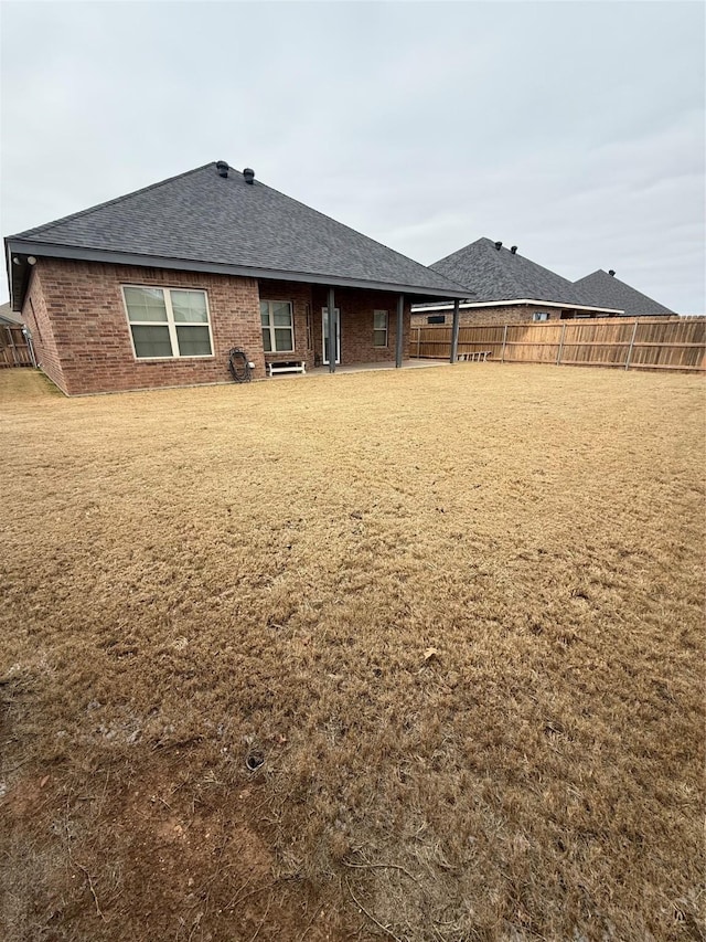 back of house with brick siding, a lawn, a shingled roof, and a fenced backyard