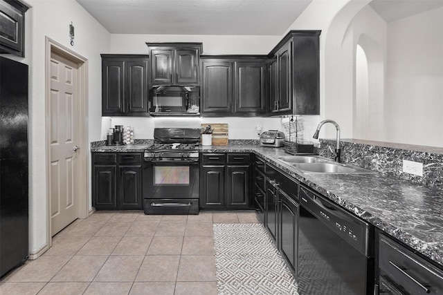 kitchen featuring black appliances, a sink, dark cabinetry, arched walkways, and light tile patterned floors