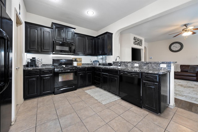 kitchen featuring black appliances, dark stone countertops, open floor plan, a peninsula, and dark cabinets