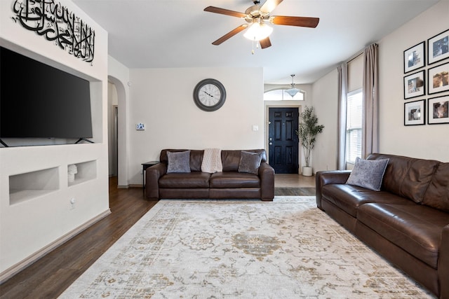 living area with a ceiling fan, wood finished floors, arched walkways, and baseboards