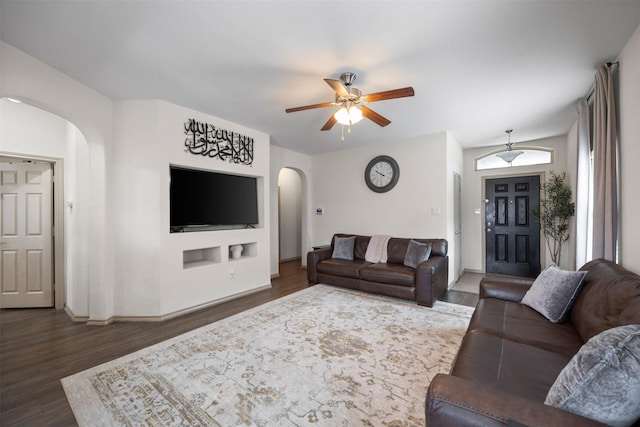 living room with baseboards, dark wood-style floors, arched walkways, and ceiling fan