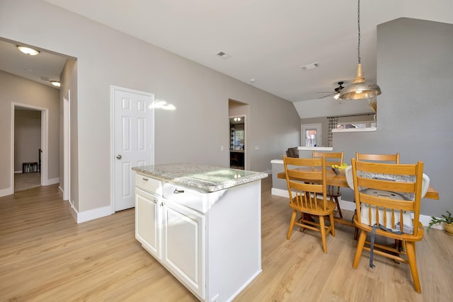 kitchen with a kitchen island, baseboards, light wood-type flooring, vaulted ceiling, and white cabinetry