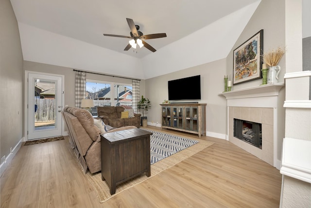 living area with ceiling fan, lofted ceiling, light wood-style flooring, and a tiled fireplace