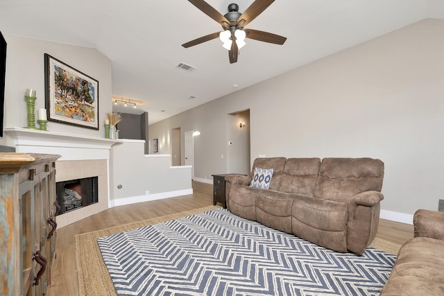 living room featuring visible vents, baseboards, a tile fireplace, light wood-style floors, and a ceiling fan