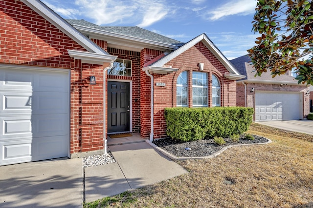 doorway to property with brick siding, driveway, a shingled roof, and a garage