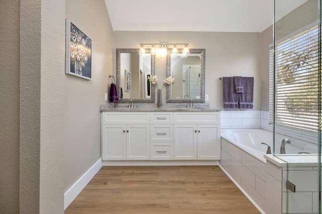 full bath featuring a sink, wood finished floors, double vanity, and a bath