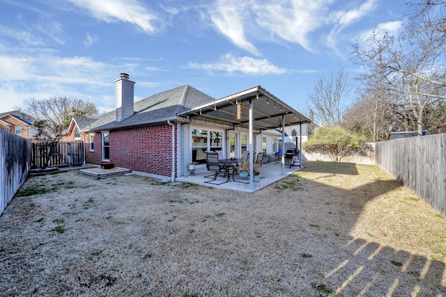 rear view of property with a patio, a fenced backyard, a shingled roof, brick siding, and a chimney