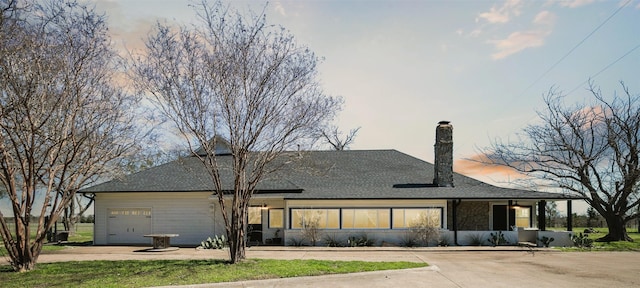 view of front facade featuring concrete driveway, an attached garage, a chimney, and a shingled roof