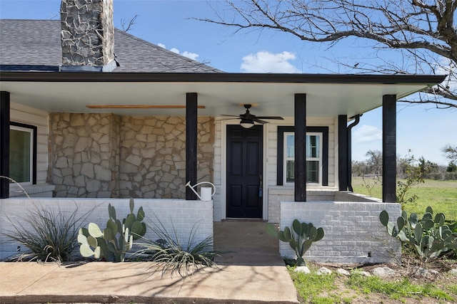 doorway to property with covered porch, stone siding, and a shingled roof