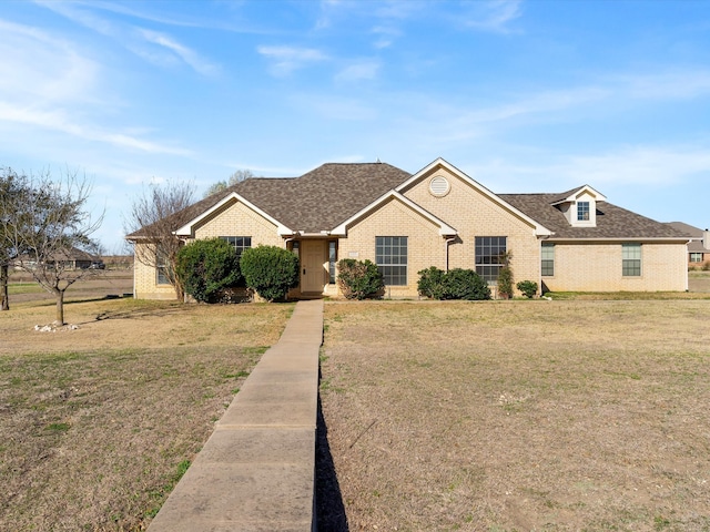 view of front of property with a front yard, brick siding, and a shingled roof