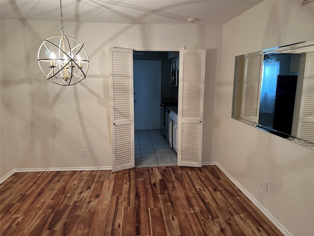 unfurnished dining area with dark wood finished floors, an inviting chandelier, and baseboards