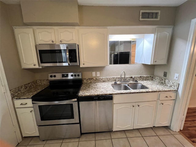 kitchen featuring visible vents, light stone countertops, white cabinets, stainless steel appliances, and a sink