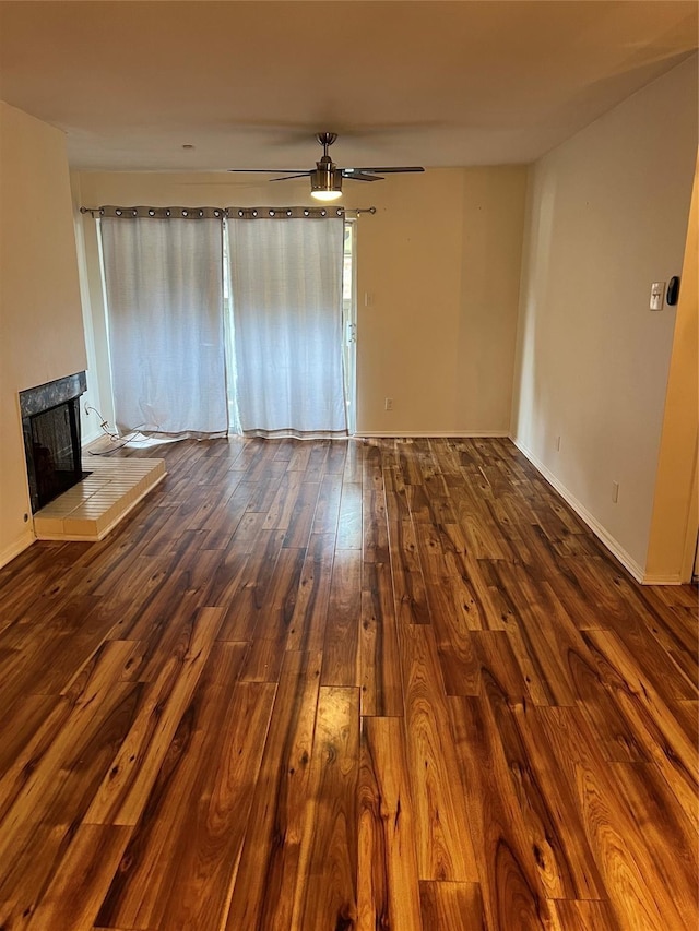 unfurnished living room featuring a tiled fireplace, baseboards, ceiling fan, and hardwood / wood-style floors