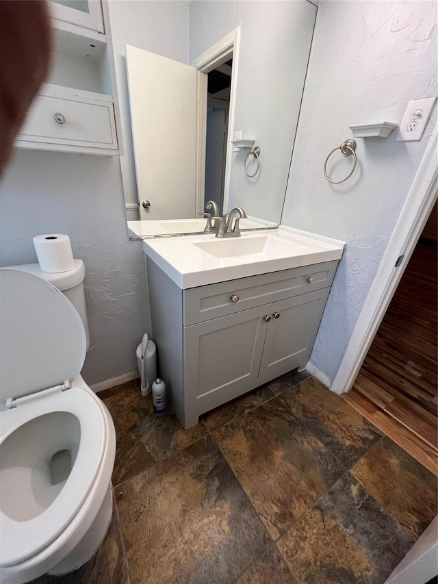 bathroom with stone finish flooring, baseboards, toilet, and vanity