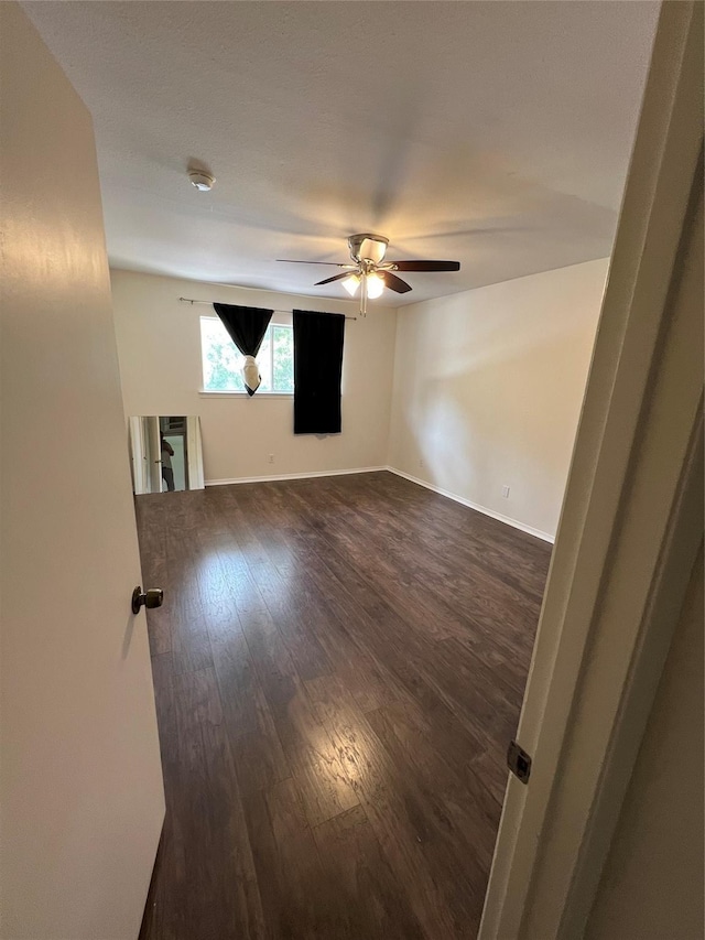 spare room with baseboards, dark wood finished floors, and a ceiling fan