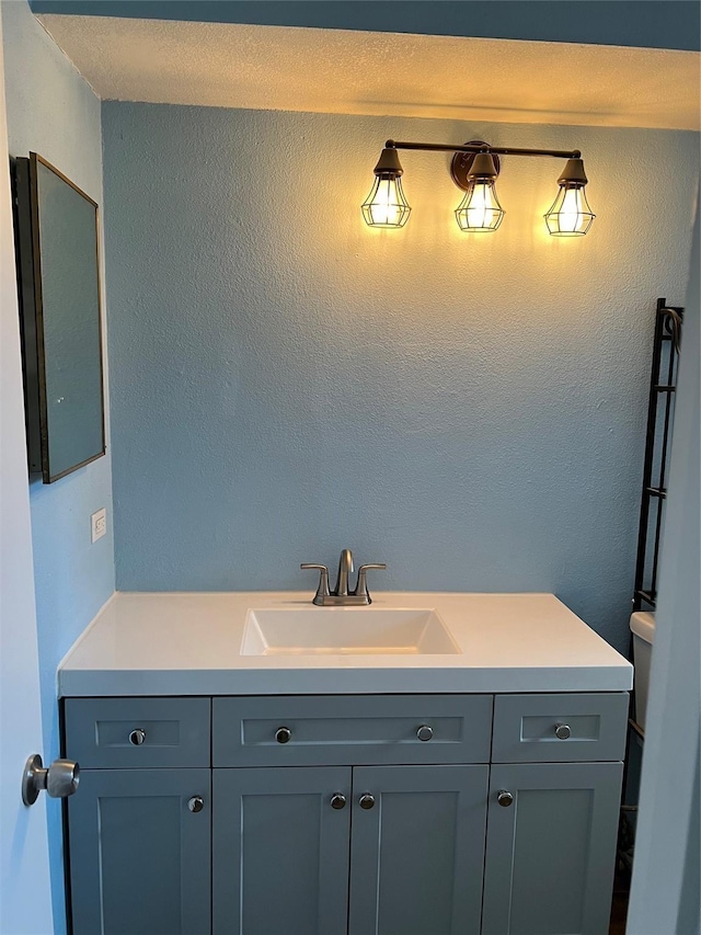 bathroom with vanity, toilet, and a textured wall