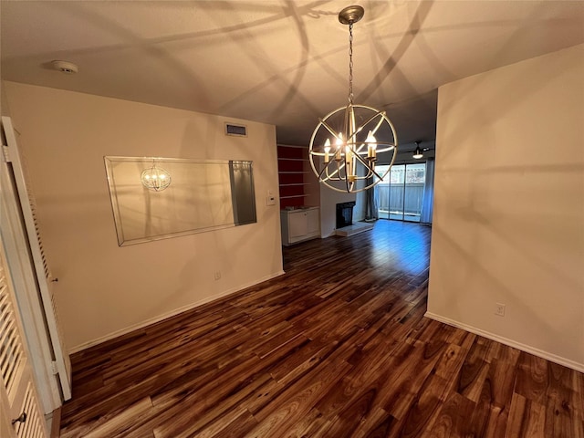 unfurnished dining area featuring visible vents, a notable chandelier, a fireplace with raised hearth, baseboards, and dark wood-style flooring