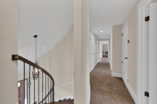 hallway with carpet, a decorative wall, a notable chandelier, and an upstairs landing