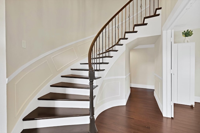 stairway with a decorative wall, wainscoting, and wood finished floors