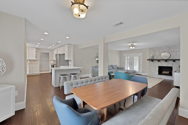 dining room with visible vents, baseboards, a stone fireplace, recessed lighting, and dark wood-style flooring