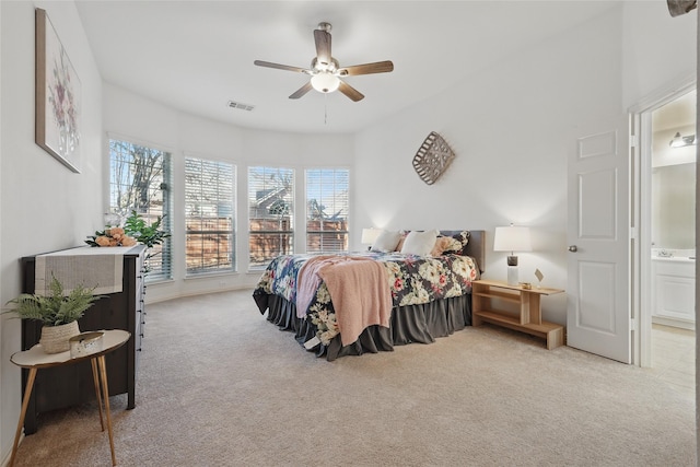 carpeted bedroom with visible vents, ensuite bathroom, and a ceiling fan