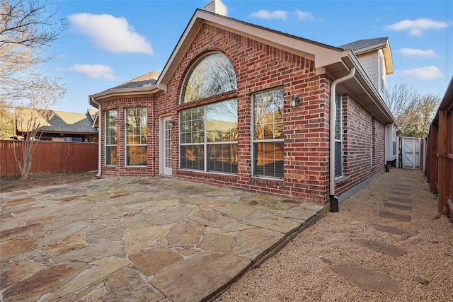 rear view of house featuring brick siding, a fenced backyard, and a patio area