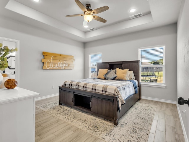 bedroom featuring visible vents, a raised ceiling, light wood-style floors, and baseboards