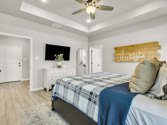 bedroom with visible vents, light wood-type flooring, a raised ceiling, and baseboards