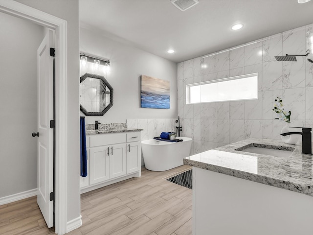 bathroom featuring visible vents, a freestanding tub, two vanities, a sink, and tiled shower