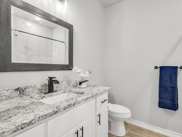 full bathroom featuring vanity, wood finished floors, baseboards, walk in shower, and toilet