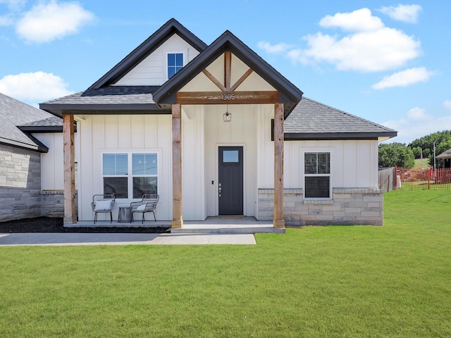 view of front of property with stone siding, board and batten siding, a shingled roof, and a front yard