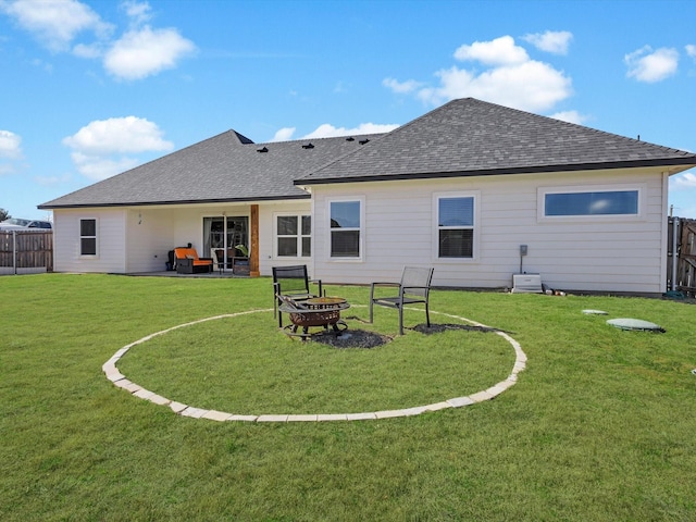 back of property with a lawn, a patio, fence, a fire pit, and roof with shingles