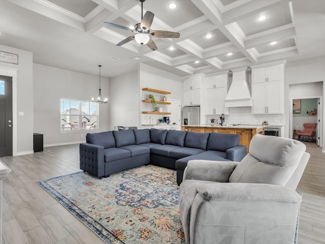 living room with beam ceiling, coffered ceiling, a towering ceiling, and ceiling fan with notable chandelier