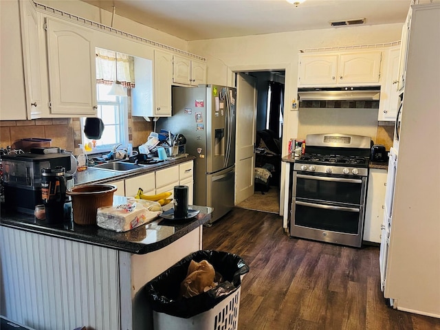 kitchen featuring under cabinet range hood, a sink, dark countertops, dark wood finished floors, and appliances with stainless steel finishes