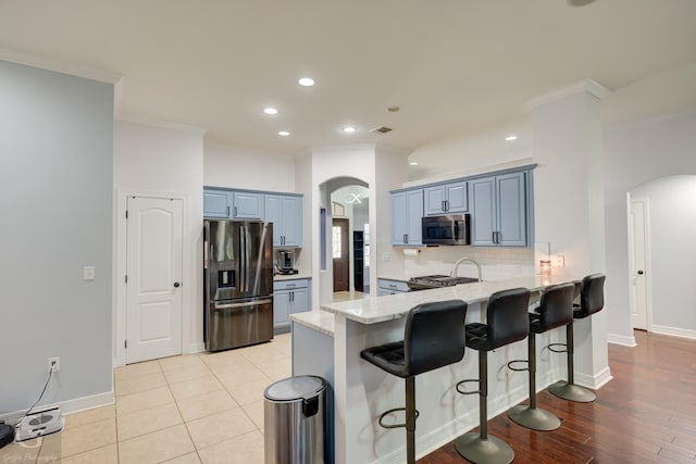 kitchen with arched walkways, stainless steel microwave, fridge with ice dispenser, and range