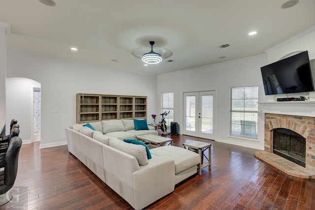 living room with dark wood-style floors, arched walkways, baseboards, a brick fireplace, and ceiling fan