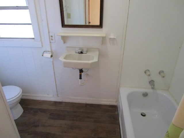 bathroom featuring baseboards, toilet, a tub to relax in, wood finished floors, and a sink