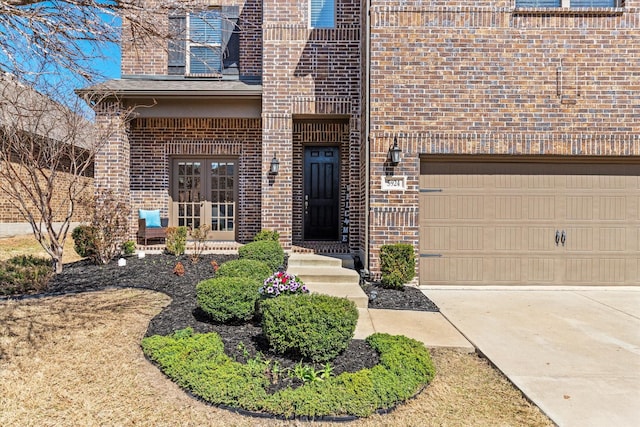 entrance to property featuring french doors, a garage, concrete driveway, and brick siding