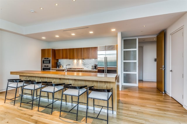 kitchen featuring brown cabinets, tasteful backsplash, appliances with stainless steel finishes, light wood finished floors, and light countertops