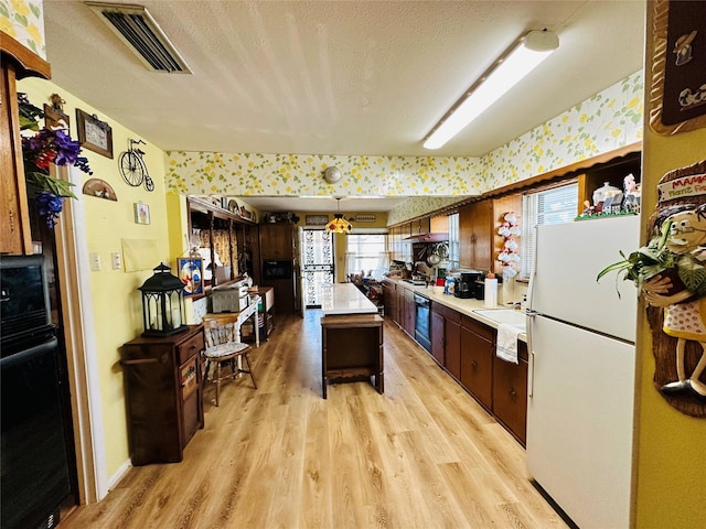 kitchen featuring visible vents, light wood-style flooring, a textured ceiling, freestanding refrigerator, and light countertops