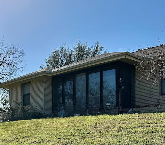 view of home's exterior with a yard, brick siding, and a sunroom