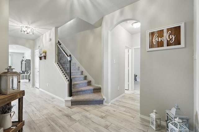 foyer with stairway, baseboards, arched walkways, and light wood-type flooring