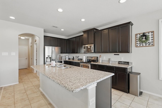 kitchen featuring a center island with sink, visible vents, arched walkways, a sink, and stainless steel appliances