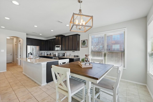 kitchen featuring an island with sink, decorative light fixtures, recessed lighting, stainless steel appliances, and arched walkways