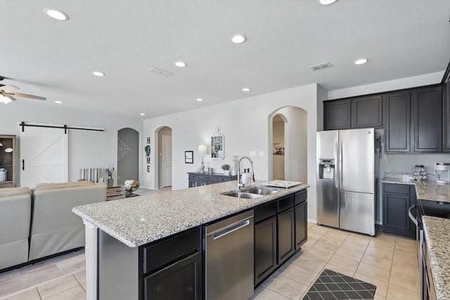 kitchen with open floor plan, a center island with sink, a barn door, appliances with stainless steel finishes, and a sink