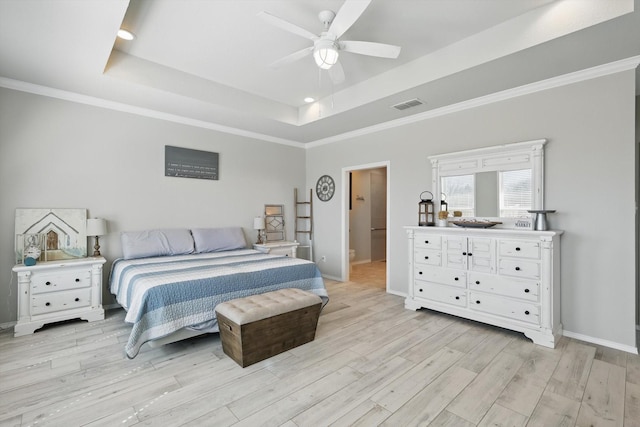 bedroom with visible vents, light wood-style flooring, ornamental molding, a tray ceiling, and baseboards