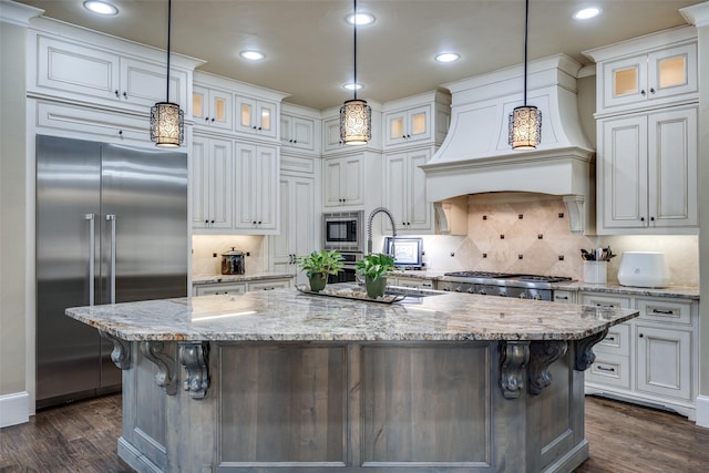 kitchen featuring premium range hood, dark wood-style flooring, white cabinets, built in appliances, and backsplash